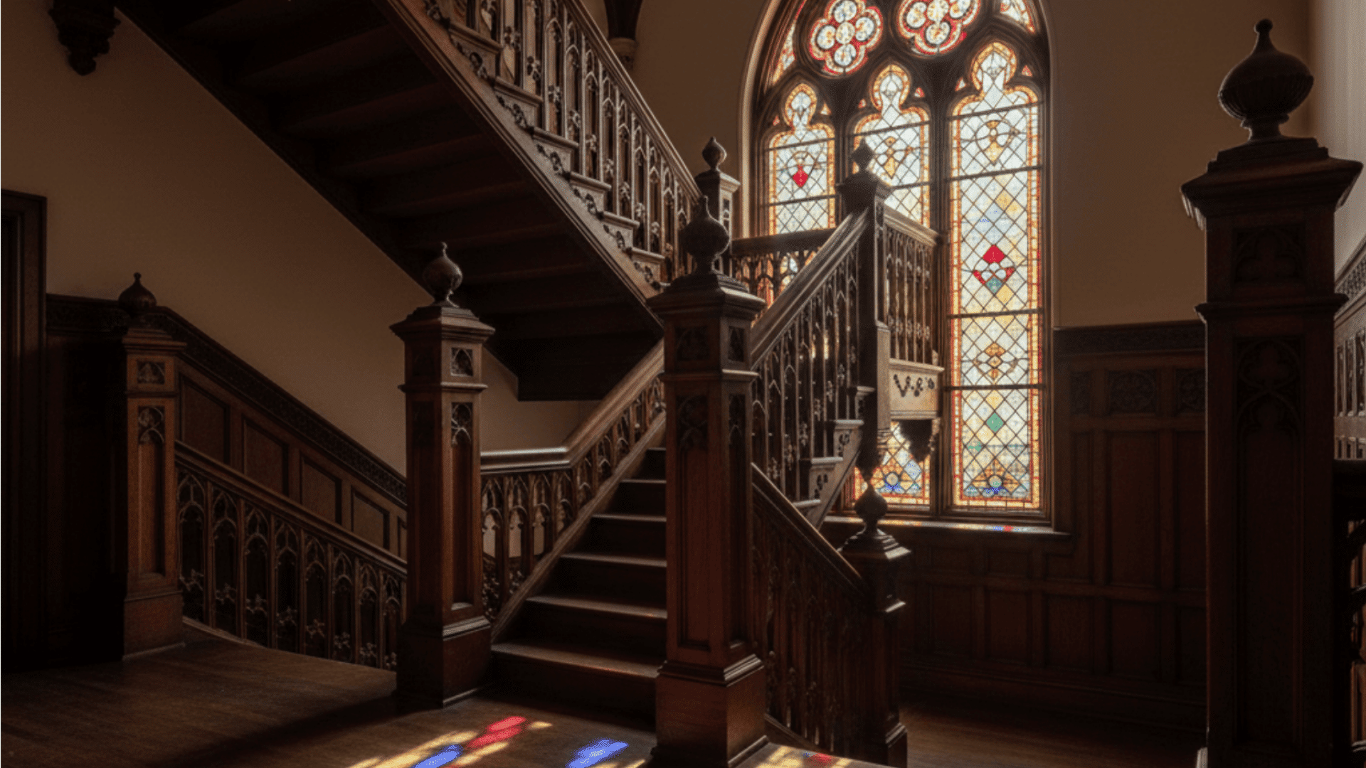 A gothic staircase featuring stained glass windows and elegant wooden railings.