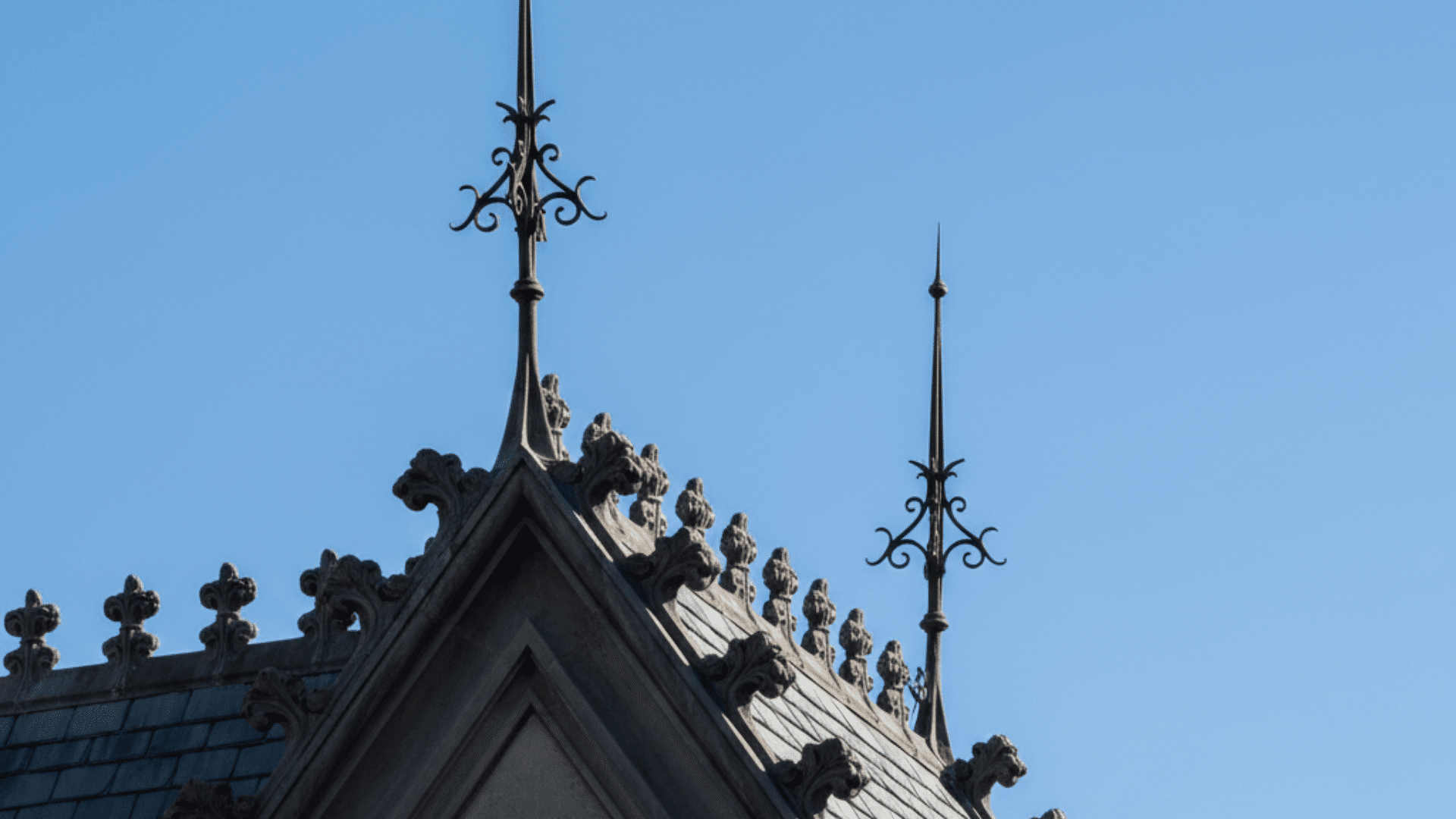 Gothic building top featuring a cross, finials, and crocket details against a clear sky, showcasing intricate architectural design.