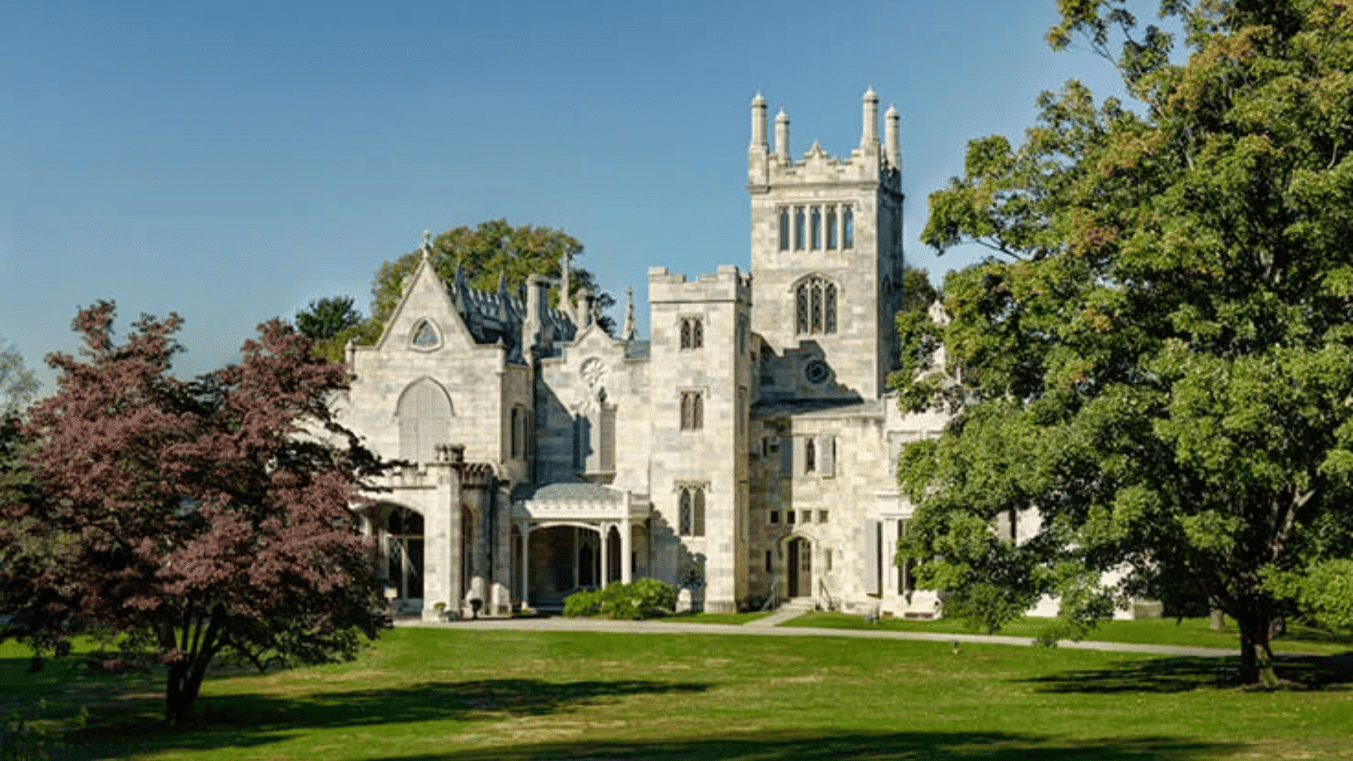 Lyndhurst Castle, a Gothic Revival mansion, is surrounded by lush trees and grass, showcasing its stunning architecture.