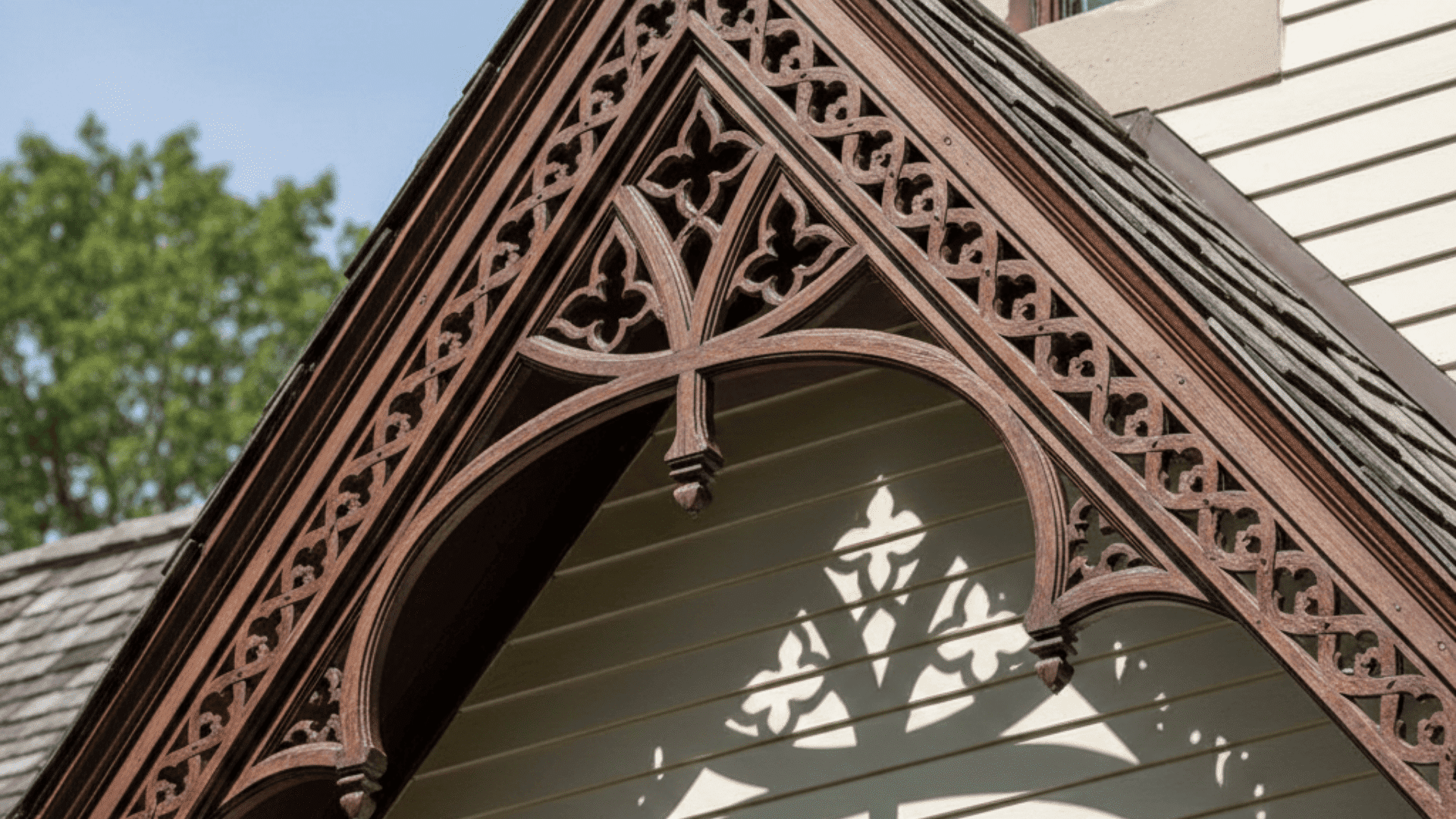 The peak of a gothic structure adorned with intricate vergeboard trim and a striking cross silhouette.