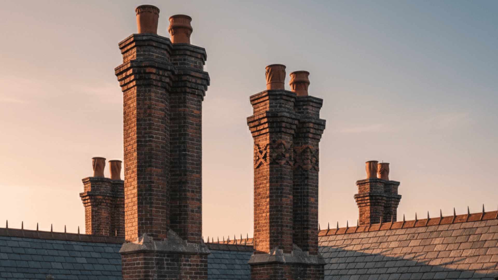 _Three gothic chimneys rise from a roof, silhouetted against a vibrant sunset sky.