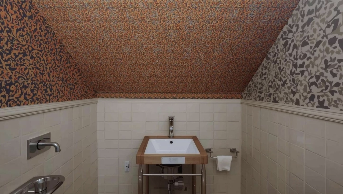 Cozy powder bath with white tile wainscoting and bold patterned wallpaper covering sloped ceiling and upper walls.