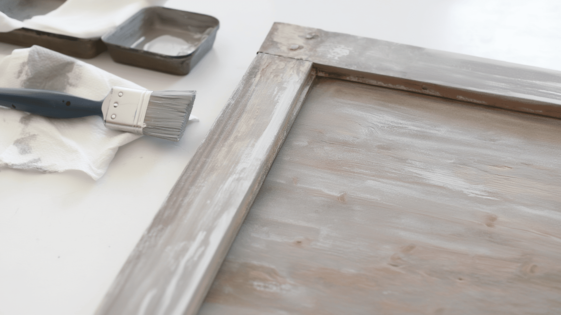 A paint brush and tray beside a frame, showcasing a dry brush weathered paint effect.