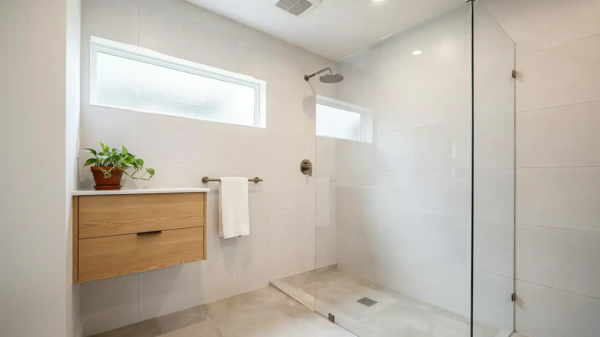 Clean, well-ventilated bathroom with white tiles, a glass shower enclosure, exhaust fan, and a hung towel.