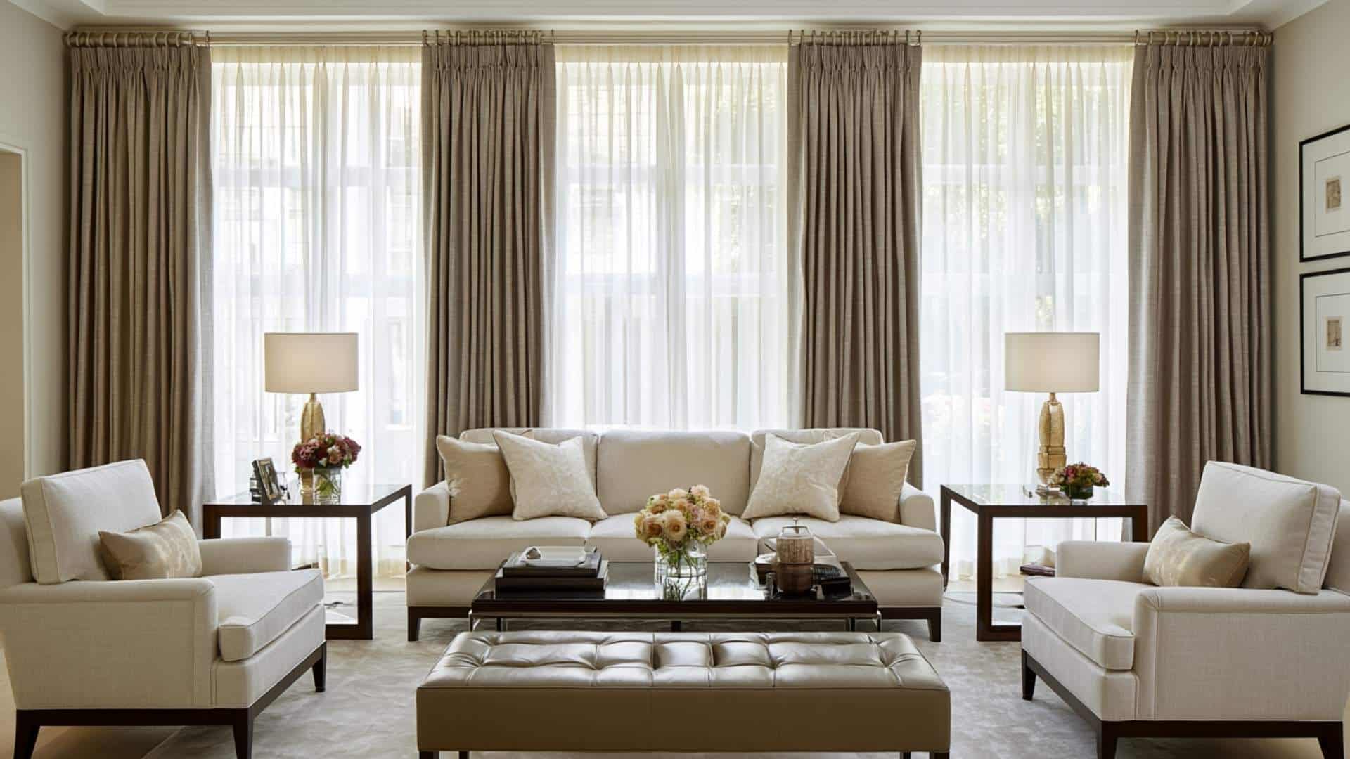 Taupe pinch pleat curtains layered over white sheers on floor-to-ceiling windows in a formal neutral living room