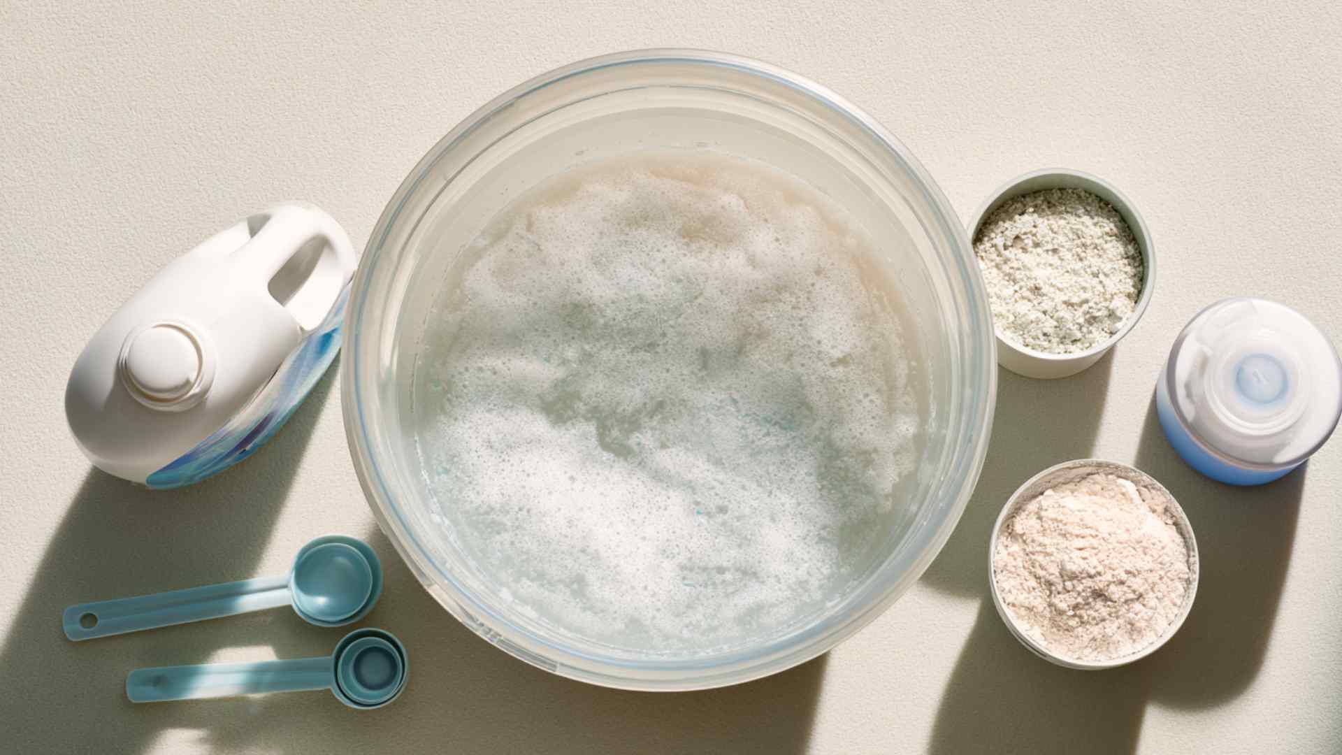 Overhead view of laundry detergent, OxiClean, and fabric softener arranged beside bucket of mixed carpet cleaner solution