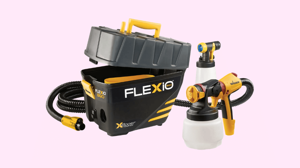 Wagner FLEXiO 5000 stationary paint sprayer system with turbine base, hoses, and spray guns with paint cups on a light pink background.